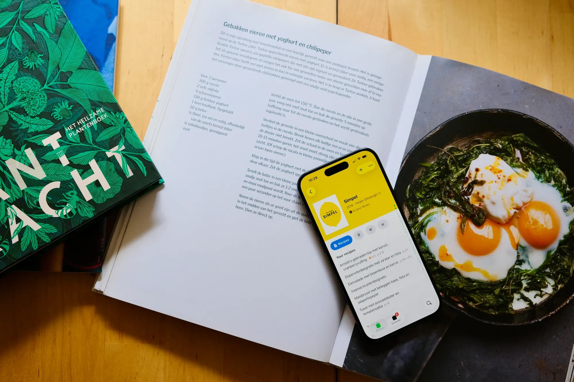 Een iPhone met Simpel van Ottolenghi in CookCook, liggend op een opengeslagen kookboek naast een foto van gebakken eieren